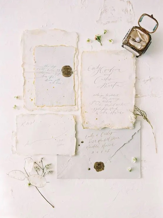 a neutral handmade paper wedding invitation suite with a raw edge and delicate calligraphy, with gold wax seals