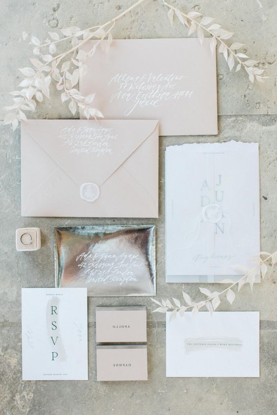 a neutral wedding invitation suite with blush envelopes, a neutral card and a shiny metallic envelope