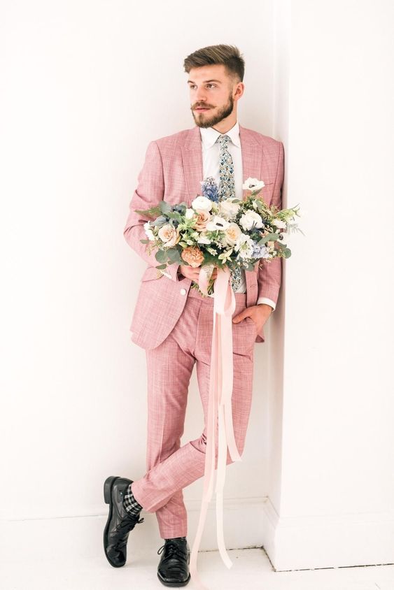 a pink pantsuit, a white shirt, black shoes and checked socks, a floral tie compsoe a whimsical look for the groom