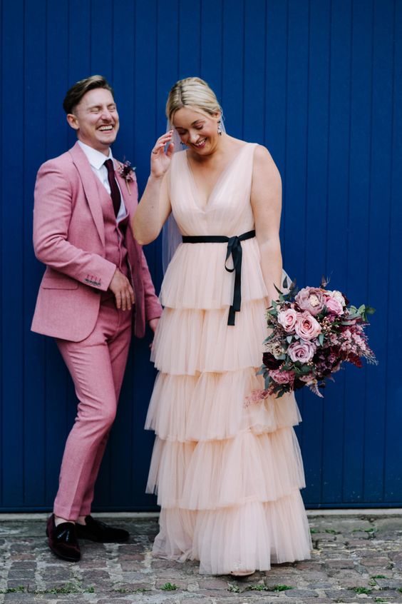 a pink three-piece pantsuit, a white shirt, a black tie and blakc loafers are a bold and catchy combo for a wedding