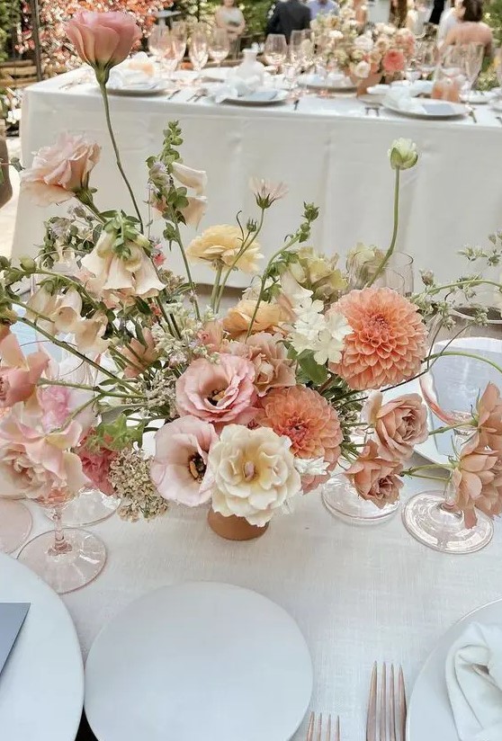 a pretty and chic textural and dimensional wedding centerpiece of orange dahlias, pink, neutral and light yellow blooms and greenery is wow