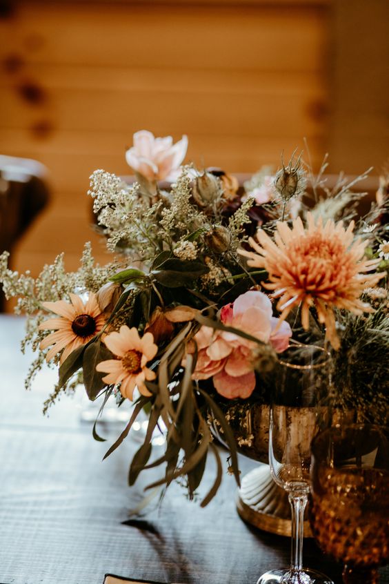 a pretty and relaxed fall wedding centerpiece of blush blooms, rust mums, greenery and some fillers is amazing