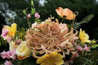 a refined and chic wedding centerpiece of pink and yellow blooms and an oversized blush chrysanthemum with a lot of greenery