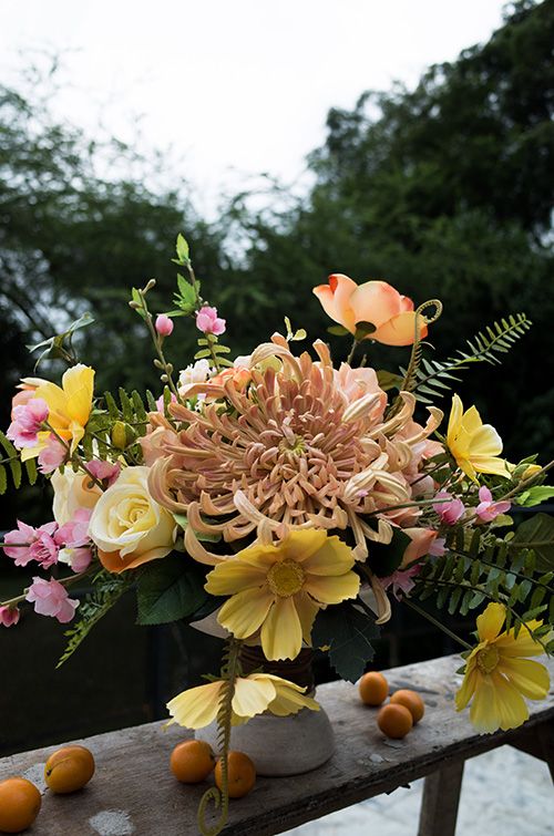 a refined and chic wedding centerpiece of pink and yellow blooms and an oversized blush chrysanthemum with a lot of greenery