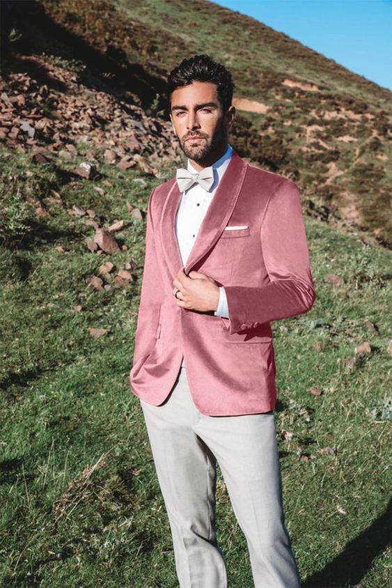 a refined groom's look with grey trousers and a bow tie, a pink velvet blazer, a white shirt with black buttons
