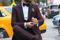 a refined purple groom’s outfit with a tuxedo and black lapels, a waistcoat, black shoes and socks, a black bow tie