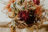 a rustic fall wedding centerpiece of orange dahlias and burgundy chrysanthemums, greenery and herbs is cool