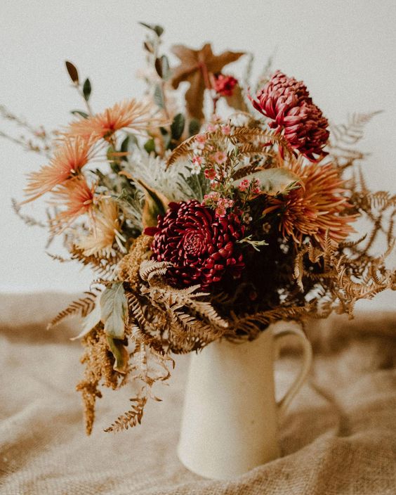 a rustic fall wedding centerpiece of orange dahlias and burgundy chrysanthemums, greenery and herbs is cool