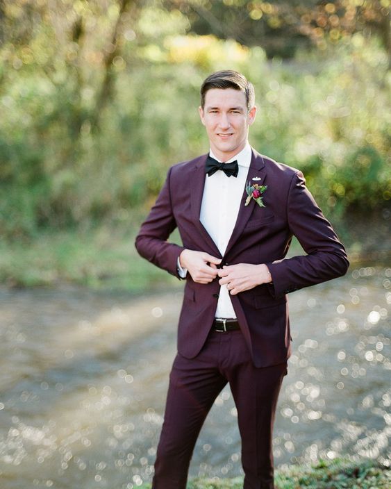 a simple and very refined groom's look with a purple pantsuit, a white shirt, a black bow tie and a belt