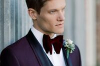a sophisticated groom’s look with a purple tux with black lapels, a white shirt, a black waistcoat and a burgundy velvet bow tie