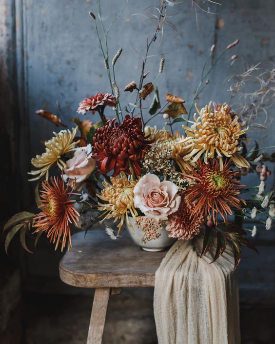 a sophisticated wedding centerpiece of blush roses, burgundy and yellow chrysanthemums and fall leaves