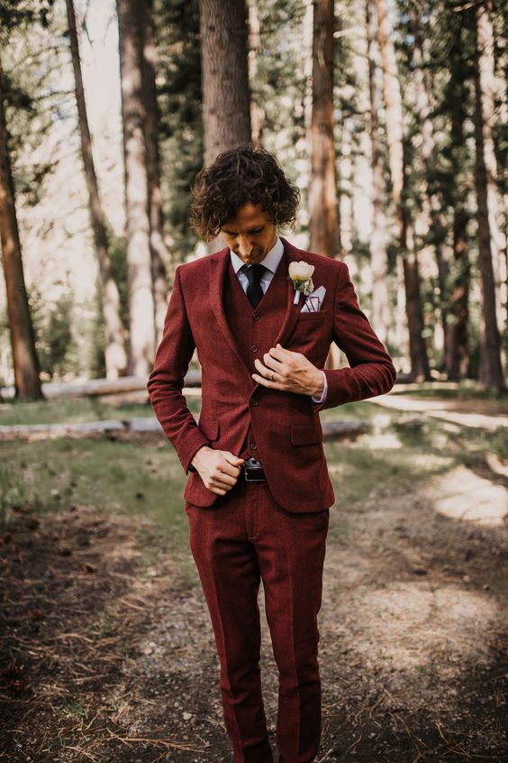 a stylish look with a burgundy three piece pantsuit, a white shirt, a black tie and a white bloom boutonniere