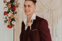 a stylish modern groom’s look with a burgundy three-piece pantsuit, a white shirt, a bold boutonniere