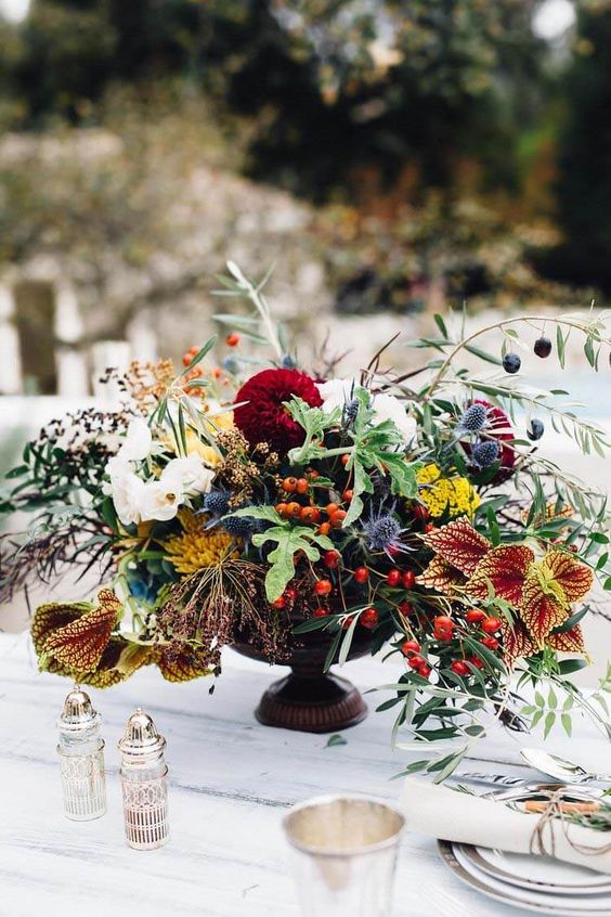 a super bold fall wedding centerpiece of white and burgundy blooms, mustard mums, greenery, berries and leaves