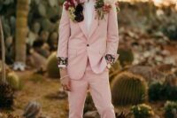 a unique boho groom’s look with a blush pantsuit, a white shirt, creamy boots, flower adorned shoulders is wow