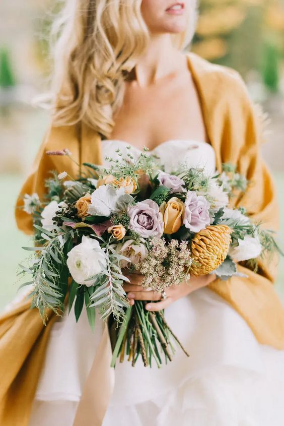 a unique fall wedding bouquet of white ranunuculus, lilac roses, mustard roses and chrysanthemums, greenery and privet berries