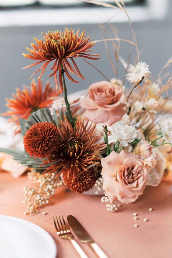 a unique wedding centerpiece of blush roses, rust dahlias and chrysanthemums, white daisies and berries