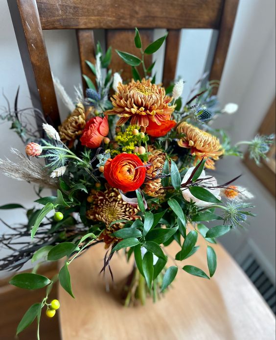 a vibrant fall wedding bouquet of rust chrysanthemums, red ranunculus, greenery and thistles is wow