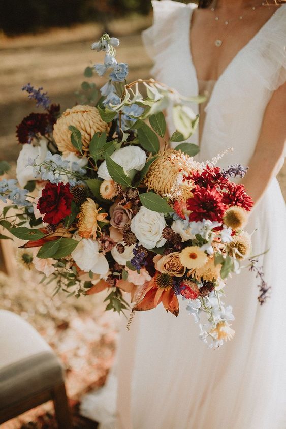 a vibrant fall wedding bouquet of yellow chrysanthemums, white and yellow roses, burgundy dahlias, greenery and blue flowers