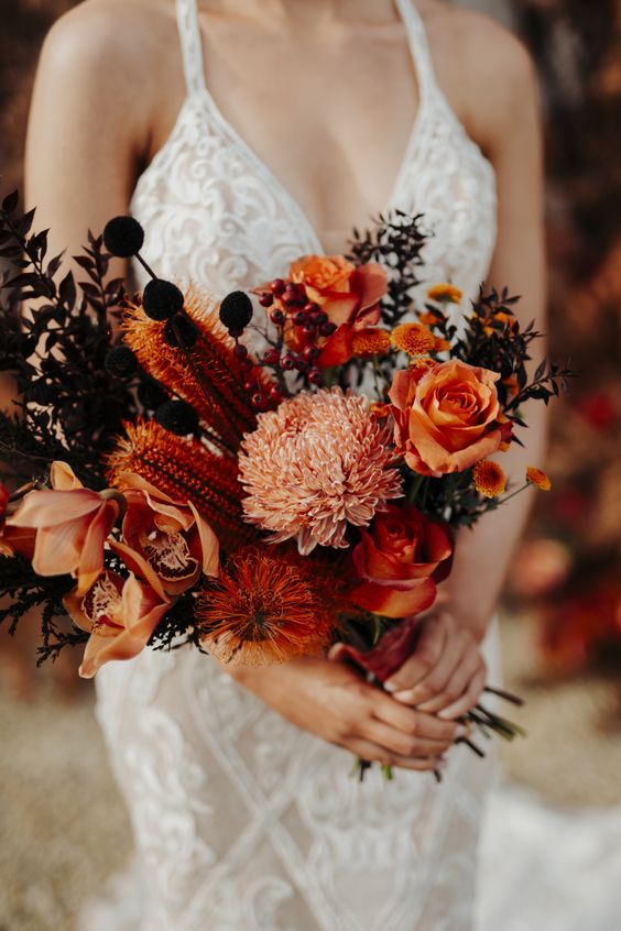 a vibrant orange wedding bouquet of roses, chrysanthemums, some orchids and other blooms, dark foliage is wow