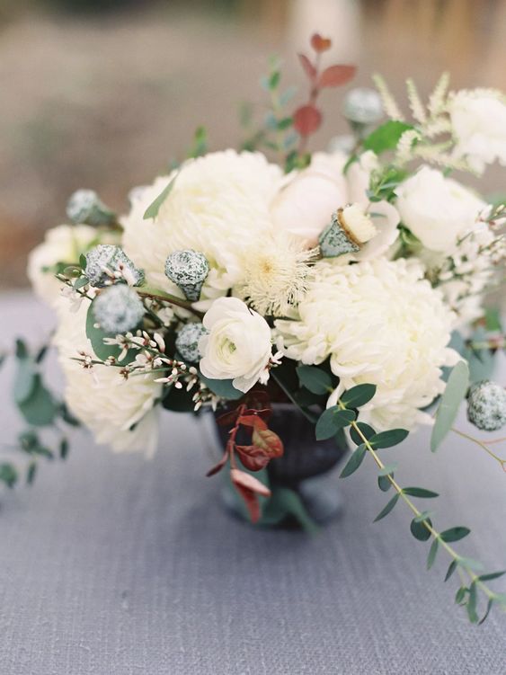 a white wedding centerpiece of mums and ranunculus, greenery and some fillers is a catchy and chic idea