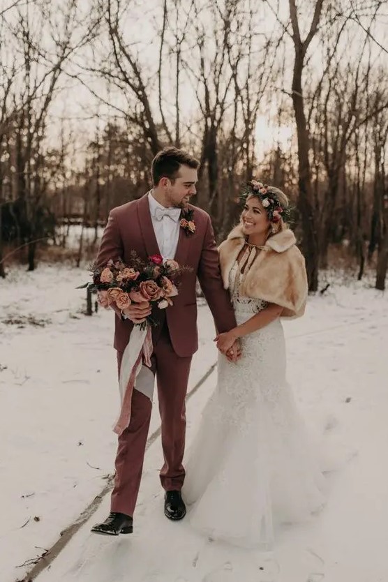 a winter groom wearing a chic mauve suit, a white shirt and a bow tie, black shoes and a blush and peach bloom boutonniere