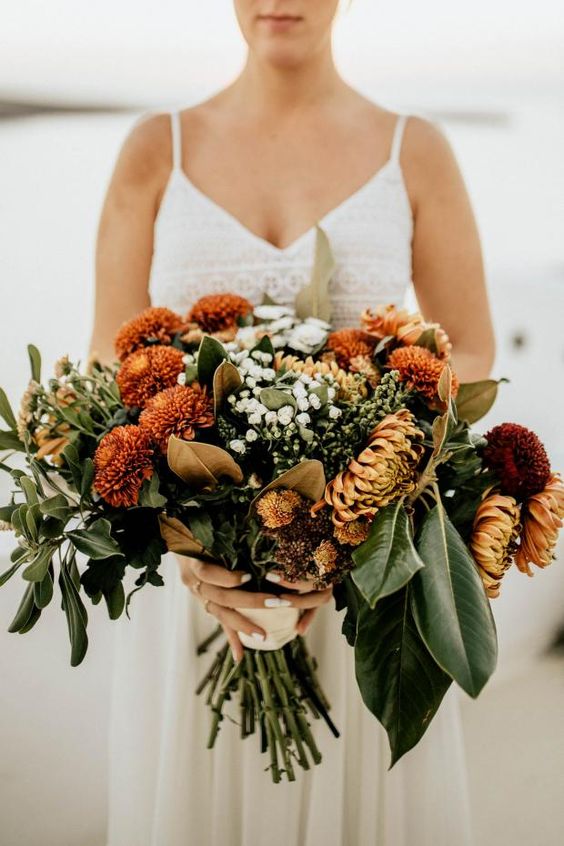 an autumnal wedding bouquet of rust-colored and orange blooms including chrysanthemums, greenery, baby's breath and foliage