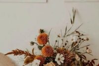 an earthy-tone wedding centerpiece of orange dahlias, coffee-colored roses, white blooms and dried flowers plus grasses