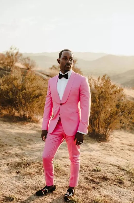 an edgy groom's look with a hot pink tuxedo, a white shirt and a black bow tie, black printed loafers just wows