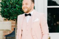 an elegant and refined groom’s look with a white shirt, a blush waistcoat, a blush blazer, a black bow tie and black pants
