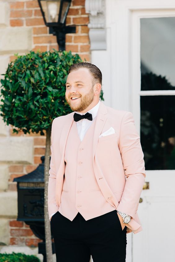 an elegant and refined groom's look with a white shirt, a blush waistcoat, a blush blazer, a black bow tie and black pants