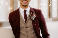 an elegant groom’s outfit with a burgundy pantsuit, a beige checked waistcoat, a white shirt, a burgundy tie and a floral boutonniere