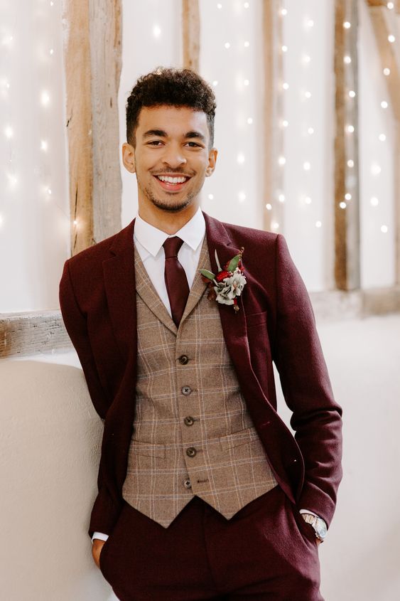 an elegant groom's outfit with a burgundy pantsuit, a beige checked waistcoat, a white shirt, a burgundy tie and a floral boutonniere