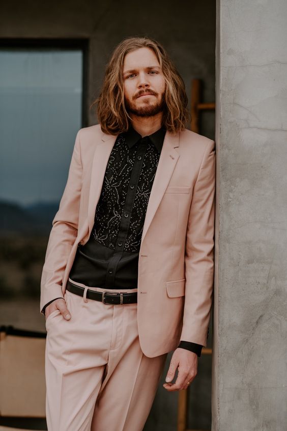 an eye-catching blush pantsuit, a black printed shirt, a black belt are a lovely look for a boho groom
