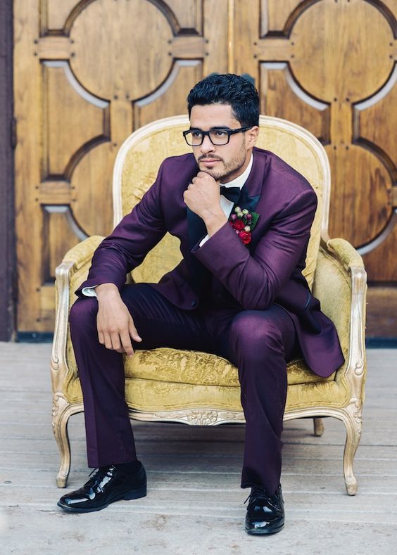 an eye-catching groom's look with a purple suit, a white shirt, a black bow tie, black shoes and a bold boutonniere