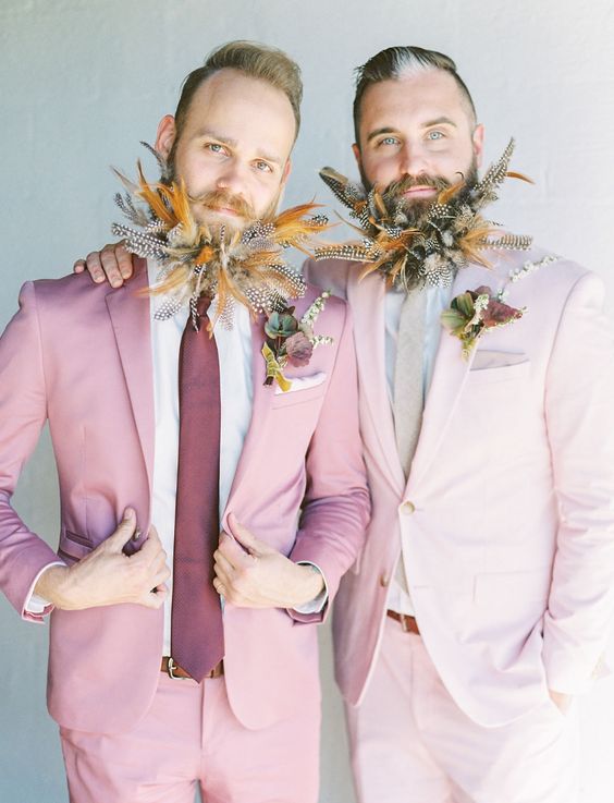 grooms wearing a blush and a light pink pantsuit, a neutral and purple tie and feather-embellished beards