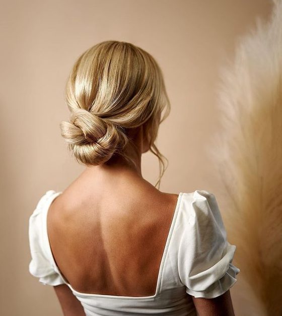 a twisted low bun with a sleek top and waves down is a stylish idea for a modern wedding, it looks chic and cool