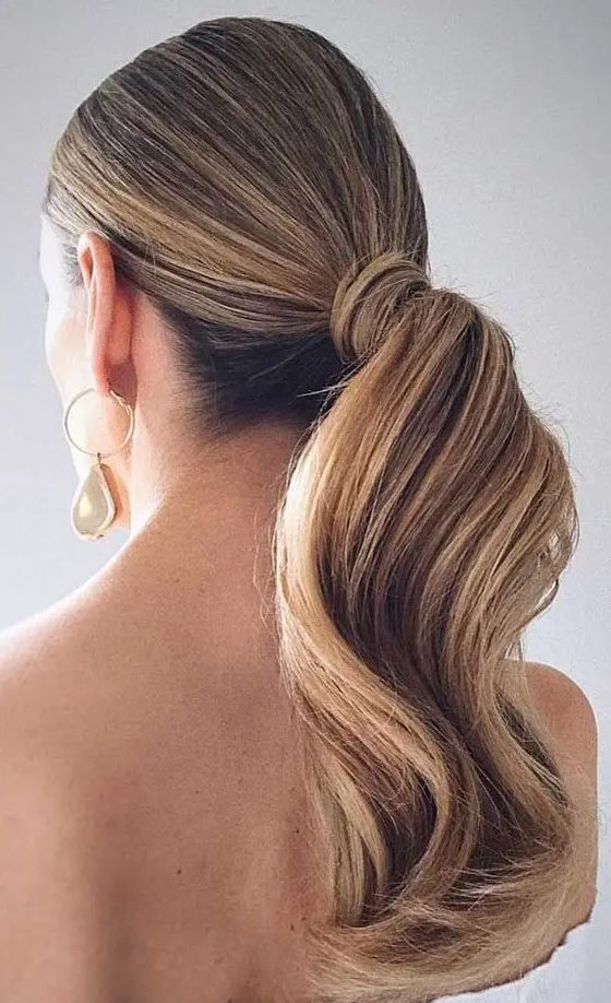 an elegant and refined low wavy ponytail with a sleek top is a stylish idea for a modern or minimalist bride, wrap the ponytail with your hair
