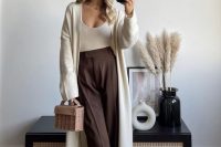 a catchy and pretty guest look with a neutral top, chocolate brown pants, a neutral maxi cardigan, a woven bag