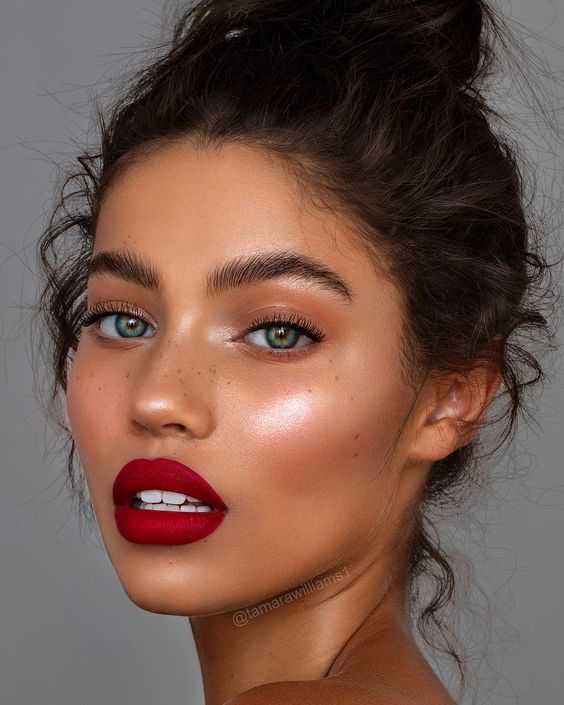 a catchy holiday makeup with a red lip, a perfect skin tone, highlighter, pink blush and fluffy eyebrows