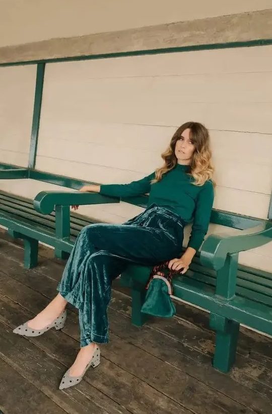 a pretty fall or winter wedding guest look with an emerald turtleneck, velvet wideleg pants, grey polka dot shoes and a small velvet bag