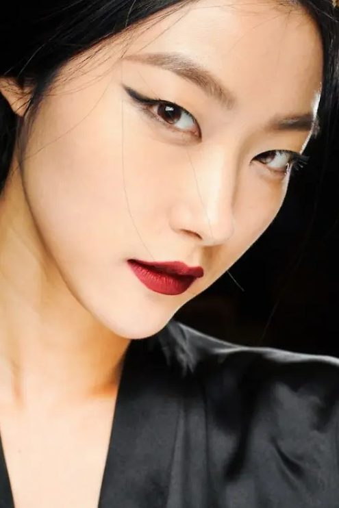 a statement makeup with black eyeliner, wide eyebrows and a bold burgundy matte lip to look fashion-forward