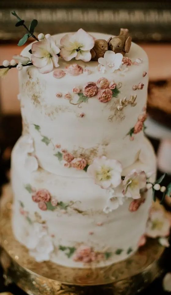 a delicate and refined white wedding cake decorated with natural and sugar blooms, with sugar leaves and birdie toppers