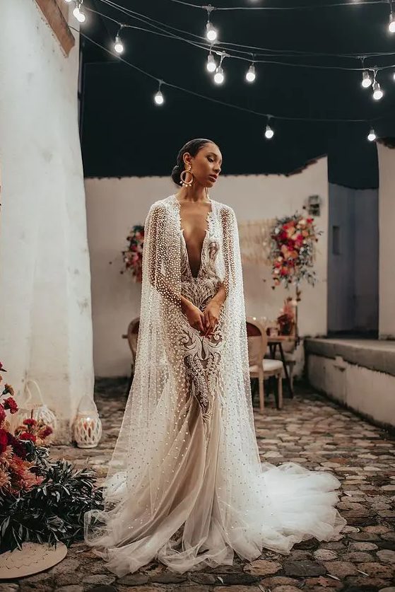 A jaw dropping lace mermaid wedding dress with a plunging neckline and a pearl and crystal long bridal capelet