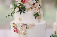 35 a white buttercream wedding cake decorated with gold foil, sugar flowers and real leaves, beads and butterflies is amazing