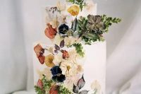 40 a sophisticated white buttercream wedding cake with pressed dried flowers and some fresh blooms and leaves attached to the cake