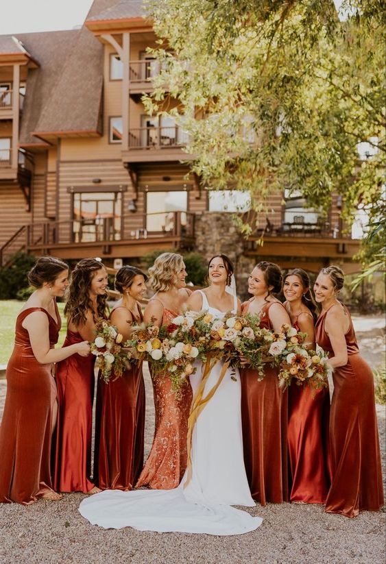 mismatching orange, burnt orange maxi bridesmaid dresses of satin and velvet for a bold fall bridal party look