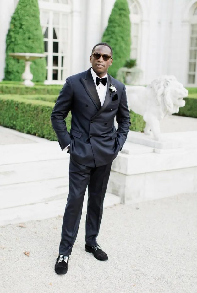 a classic navy, almost black tux with black lapels, black and white shoes, a white shirt, a white rose and sunglasses