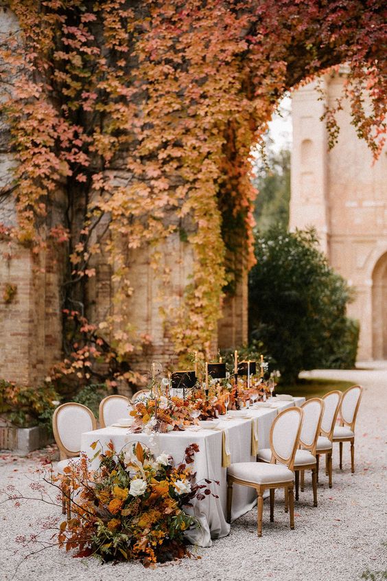 a gorgeous autumnal wedding reception space with red and yellow leaves on the wall and the same arrangements on the table