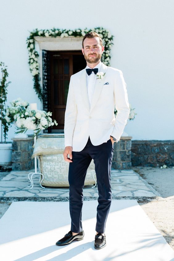 a chic white tux, a white shirt, a black bow tie, black pants and black loafers for a neutral refined wedding